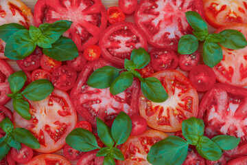 Cut tomatoes of different sorts with basil on wooden table, flat lay