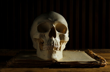 Human skull and old book on wooden table, space for text