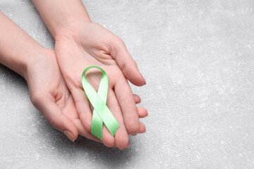 World Mental Health Day. Woman holding green ribbon on light grey background, closeup with space...
