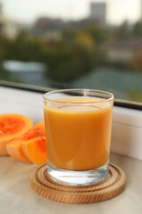 Tasty pumpkin juice in glass and cut pumpkin on windowsill indoors