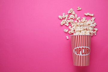 Overturned paper cup with delicious popcorn on pink background, flat lay. Space for text - obrazy, fototapety, plakaty