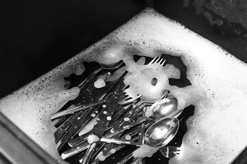Washing silver spoons, forks and knives in kitchen sink with foam, above view