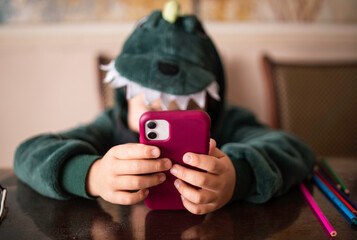 boy who looks into the phone sitting in a dinosaur costume at the table. Unrecognizable face