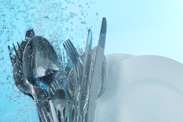 Washing silver cutlery and plates in water on light blue background