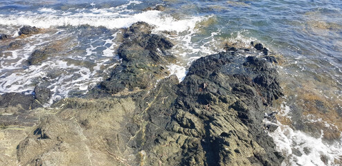 Panorama of the sea with black stones and waves.