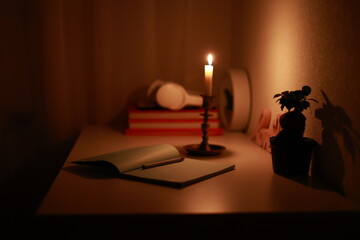 In the dark room, burning candle in candlestick is lighting on the work desk where the paper...