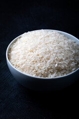 White bowl containing uncooked white rice against a black background.
