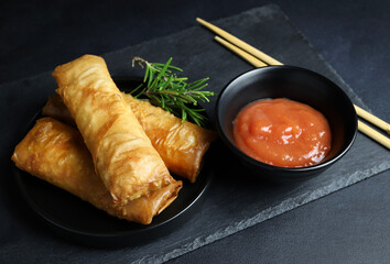 Involtini primavera fritti con salsa di peperoncino dolce su sfondo scuro. Cucina asiatica.