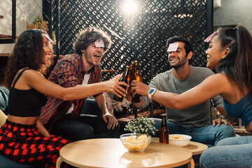 Group of happy male and female friends playing name game and raising a toast with beer bottle while sitting at home during housewarming party