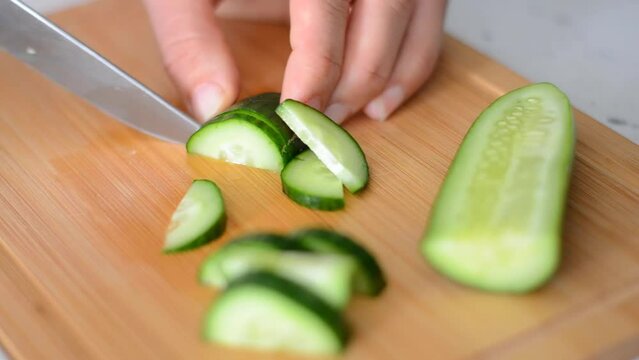 slicing cucumber, close up video of lengthwise cut cucumber being cut in half and slicing