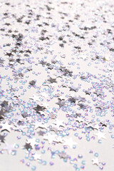 Glowing silver stars and crystals confetti scattered on a blue pastel background. Selective focus.