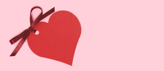 Banner with red empty tag in a heart shape with tied ribbon bow on a pink background. Composition...