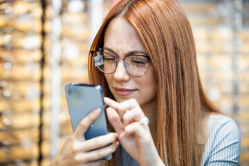 A young woman chooses glasses in an optical shop.