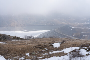 View of frozen lake and dam with road in the mountains, fog, low clouds, Mont Cenis (Moncenisio)