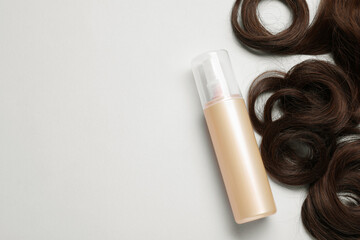 Spray bottle with thermal protection and lock of brown hair on light grey background, flat lay. Space for text
