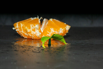 Cut tangerine with splashes of water on a black background.