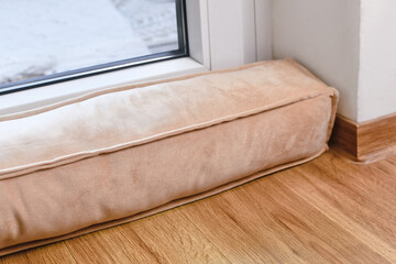 Draft excluder lying in front of door to keep out cold air and save energy for heating in room - obrazy, fototapety, plakaty