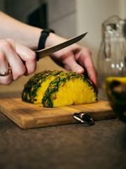 a woman cuts a pineapple on a wooden board with a knife. cooking a dish with pineapple. slicing pineapple on a chopping board. 