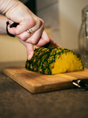 a woman cuts a pineapple on a wooden board with a knife. cooking a dish with pineapple. slicing pineapple on a chopping board. 