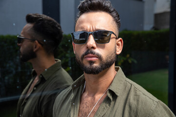 Obraz premium young bearded man wearing sunglasses looking at camera, photo taken outdoors, reflection appearing to the side, copy space