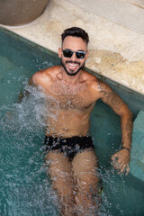 handsome muscular man in the pool, man with a beard, swimming trunks and tattoos in the water
