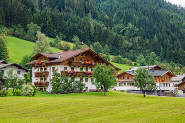 Fototapeta na wymiar Traditional alpine houses with flowers on balcony in summer, landscape of Austrian Alps, village of Grossarl, Land Salzburg.