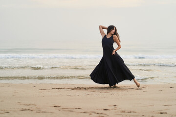 Fototapeta na wymiar a woman dancing in a black dress on the shore of the ocean expressing strength and determination