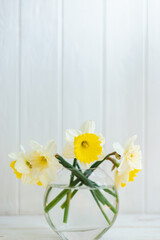 Yellow flowers in a glass vase on a white wooden background
