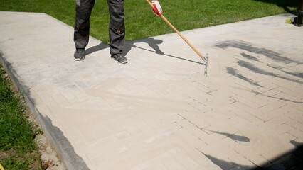 Pointing a patio with dry grouting cement grouting mix. Seeded fine sand on paving slabs - grouting. Sand with the help of the rule is rubbed into the seams of paving slabs. Grouting paving slabs. - obrazy, fototapety, plakaty