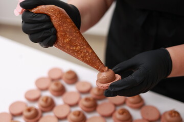 Close up of chef hands putting salt caramel with nuts in ganache cream on chocolate macarons...