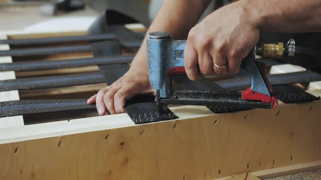 A worker makes a sofa in a furniture factory. Close-up of a carpenter working with a pneumatic pistol, slow motion.
