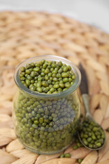Glass jar of mung beans with spoon on wicker mat, closeup