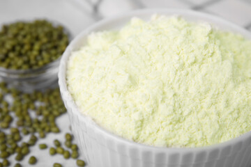 Mung bean flour in bowl and seeds on white table, closeup