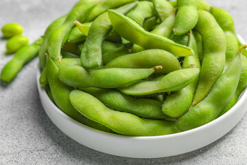 Plate with green edamame beans in pods on light grey table, closeup