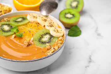Bowl of delicious fruit smoothie with fresh banana, kiwi slices and granola served on white marble table, closeup. Space for text