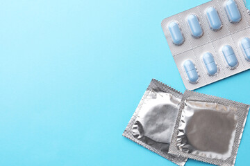 Pills and condoms on light blue background, flat lay with space for text. Potency problem
