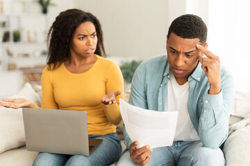 Angry unhappy millennial african american lady quarreling at guy over debts and bills with laptop