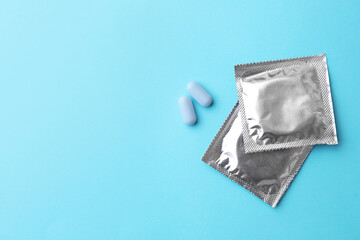 Pills and condoms on light blue background, flat lay with space for text. Potency problem