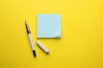 Paper note and pen on yellow background, flat lay. Space for text