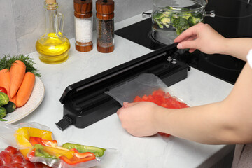 Woman using sealer for vacuum packing with plastic bag of red pepper at white table, closeup