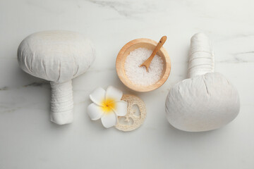 Flat lay composition with spa bags, sea salt and plumeria flower on white marble table