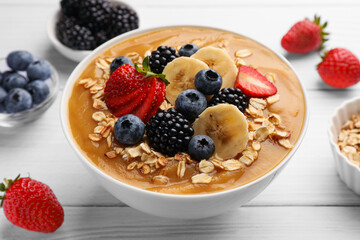 Delicious smoothie bowl with fresh berries, banana and oatmeal on white wooden table, closeup