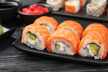 Tasty sushi rolls with salmon on black wooden table, closeup