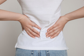 Woman suffering from back pain on light grey background, closeup. Arthritis symptoms