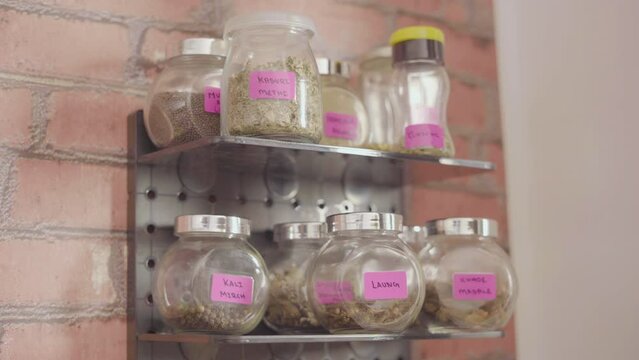 Close up of unknown female hand picking masala glass jar in kitchen. Indian food. Translation: Indian kitchen spices name written in Roman Hindi