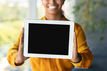 Happy black businesswoman holding digital tablet with blank screen posing in office interior, free space, mockup