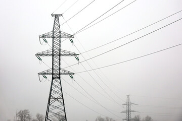 High voltage towers with electrical wires on sky background in fog. Electricity transmission lines...