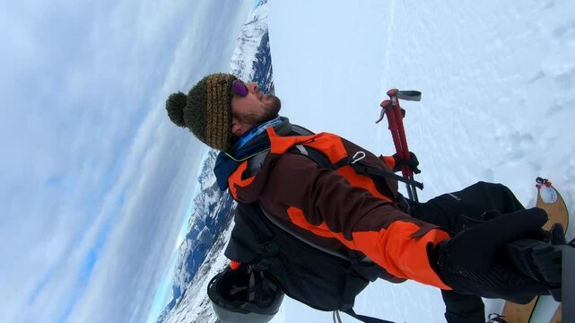side vertical video of a male caucasian splitboarder with orange jacket, black backpack and winter hat hiking in french alps, devoluy valley to the submit "le Chauvet" in december 2022
