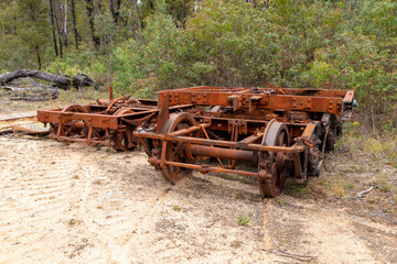 Photograph of old and rusty train bogie wheels and parts of the undercarriage and springs that have been left dormant on brown dirt in a forest