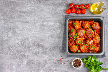 Homemade meatballs with tomato sauce and spices served in black pan on grey background. Tasty cooked meat balls made with minced beef and food ingredients. Top View, Flat lay, banner with copy space